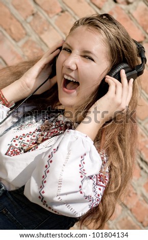 Teenager girl in headphones or portrait of a beautiful young woman smiling and listening to earphones on brick wall background