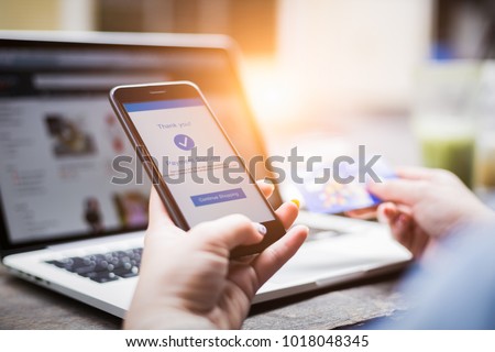 Online shopping concept, young woman hands holding mobile phone showing payment success information on screen with credit card and laptop computer on table while relax at home Royalty-Free Stock Photo #1018048345