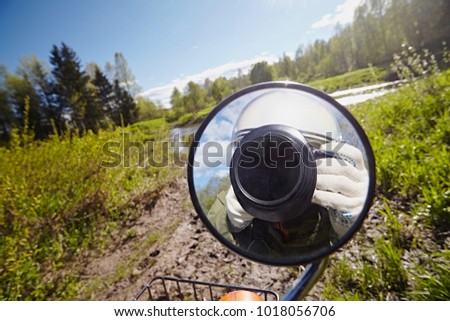 Reflections of the photographer in a motorcycle mirror with a white helmet. A man with a camera takes pictures through a glass on a nature background.
