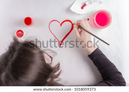 St. Valentine's Day background. Girl drawing with paints heart on white background.Card concept.Copy space