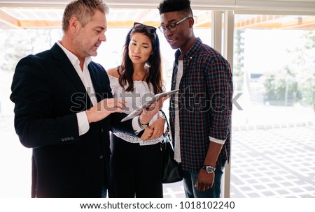 Realtor showing terms of contract on tablet to interracial couple. Real estate agent sharing property details with clients. Royalty-Free Stock Photo #1018102240