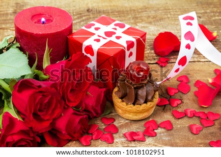 Cupcake with cherry  in front of bouquet of red roses and candles on wooden background. Valentines day concept. Focus on cake.