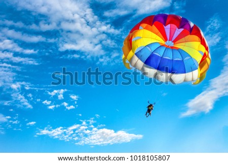 Two men are flying in the blue sky using a colorful parachute. Royalty-Free Stock Photo #1018105807