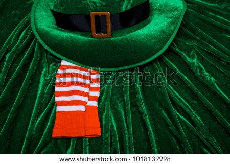 A St. Patrick's day costume hat of a leprechaun. Green Irish hat is on a green background with orange striped socks.