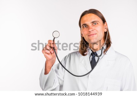 Portrait of a young friendly smiling male doctor dressed in beautiful uniform with stethoscope and medicine pills on abstract blurred white background. Healthcare medical and pharmaceutical concept