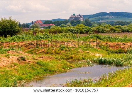 Beautiful scenery of Olesko Castle and apuchin Monastery with small pond and fields on foreground.