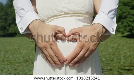 CLOSE UP Unrecognizable couple makes heart shape across woman's pregnant belly with their hands. Expecting parents gesture their excitement for soon to be born baby. Loving partners enjoying pregnancy