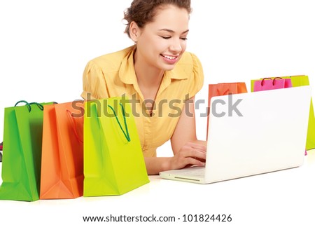 Young girl sitting with laptop near shopping bag, isolated on white background