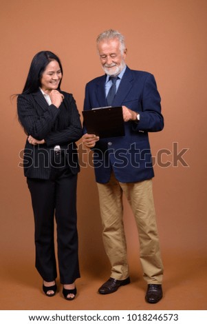 Studio shot of senior businessman and mature Asian businesswoman together against brown background