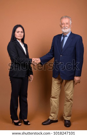 Studio shot of senior businessman and mature Asian businesswoman together against brown background