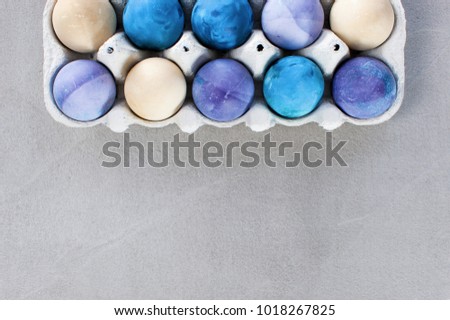 Background with blue and violet easter eggs in the box on the textured gray table. Copy space