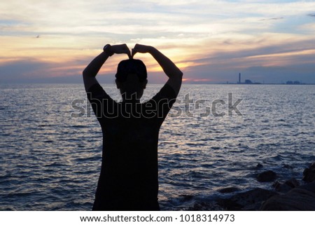 A woman is standing at the beach and making her arms like a heart. The picture concepts are love the sea, valentine, traveling with copy space.