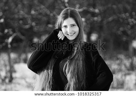 A fashion model in a black dress in the winter in the yard puts on a photo shoot.Black and white photo.