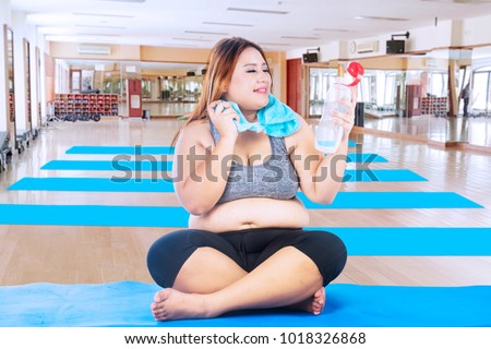 Picture of Caucasian fat woman holding a bottle of water while resting on the mat, Shot in the fitness center