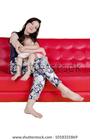 Caucasian woman smiling at the camera while embracing her daughter and sitting on the couch, isolated on white background
