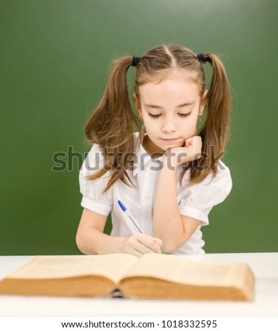 Little  girl with book preparing for the exam on the background of a school board