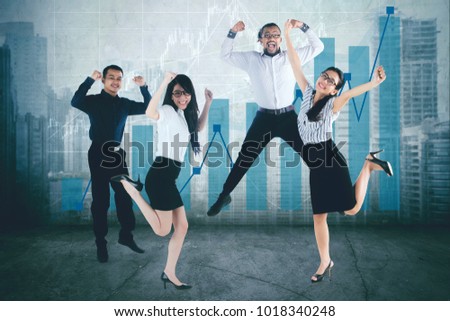Group of diversity business team jumping together while celebrating their success, shot with growth finance chart background