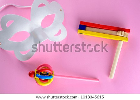 Purim Jewish carnival holiday celebration concept. Colorful wooden noisemakers or graggers and white venetian mask on pink background.Top view.Flat lay. 