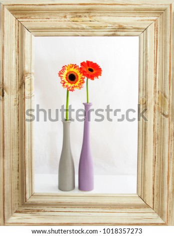 Two gerbera flowers in vases on a wooden frame