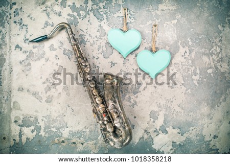 Aged retro saxophone and handmade wooden Valentine's day love hearts hanging on grunge textured concrete wall background. Vintage old style filtered photo