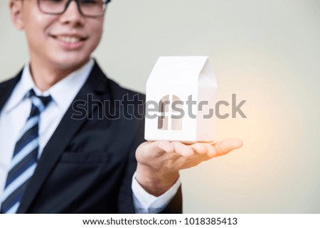 Young business man in dark suite, Close up hand with model of house. Business success, businessman on background. Select focus and use effect filter.