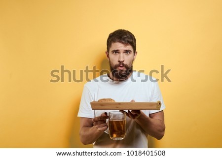  surprised man with a beard holding a tray with fast food, a mug of beer on a yellow background                             