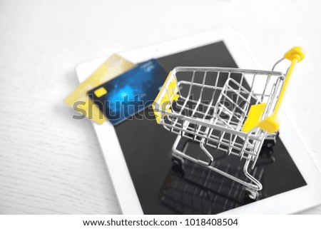 Tablet computer, small shopping trolley and credit cards on table, closeup. Internet shopping concept