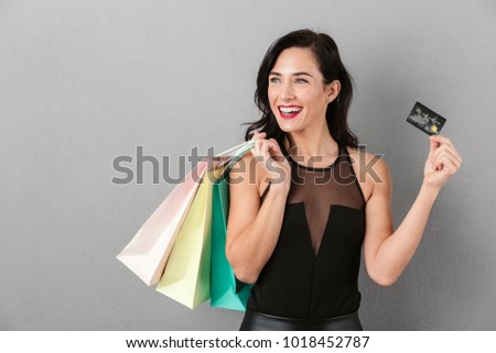 Portrait of a laughing woman dressed in skirt holding shopping bags and a credit card isolated over gray background