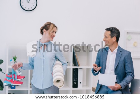 attractive businesswoman with fitness equipment talking with colleague at office