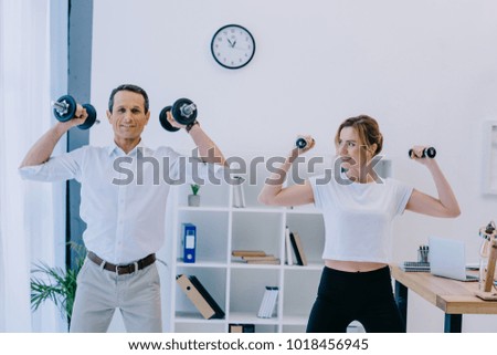 businessman with his beautiful personal trainer working out with dumbbells at office