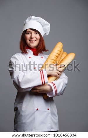 Photo of brunette chef in white coat and cap with French baguettes in hands