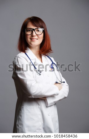 Photo of smiling female doctor in white lab coat and with phonendoscope in glasses