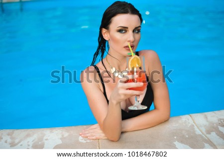 Young woman drink alcohol cocktail with orange on a swimming pool