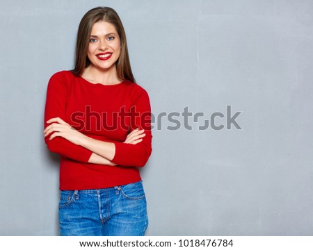 Portrait of smiling woman in red with long hair standing on gray wall background.
