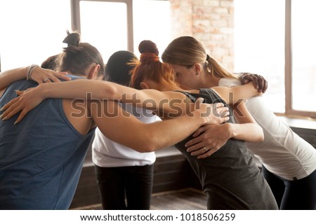 Young diverse people embracing uniting in circle standing together indoors, multiracial team of black and white friends hugging promising help support in common goal achievement, group unity concept Royalty-Free Stock Photo #1018506259