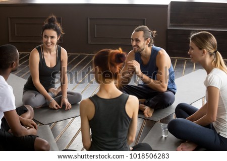 Sporty happy multi-ethnic people sitting on mats after group meditation relaxing talking about healthy life motivation before training class, discussion at yoga seminar for self-improvement concept Royalty-Free Stock Photo #1018506283