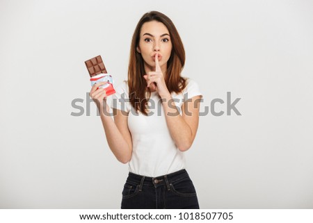 Portrait of a pretty young woman showing silence gesture while holding chocolate bar isolated over white background Royalty-Free Stock Photo #1018507705