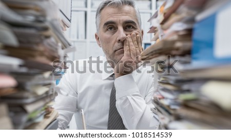 Frustrated overwhelmed executive working in the office and overloaded with paperwork, he is leaning on his arm and feeling depressed Royalty-Free Stock Photo #1018514539