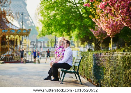 Beautiful romantic couple under blooming cherry tree on a spring day with Eiffel tower in background in Paris, France