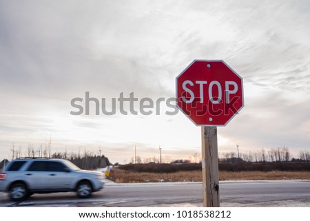 Stop Sign at an Intersection at Sunset with a Passing Car in Background