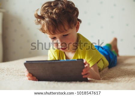 Cute little boy using a pad. Child playing with digital tablet lying on a bed. Free time. Tehnology and internet concept Royalty-Free Stock Photo #1018547617
