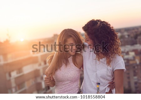 Lesbian couple standing and hugging on a building rooftop at sunset, affectionate and happy, with cityscape in the background Royalty-Free Stock Photo #1018558804