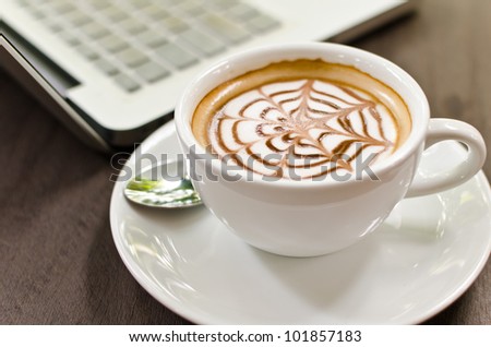 Coffee cup and laptop on the wood texture, selective focus on coffee cream.