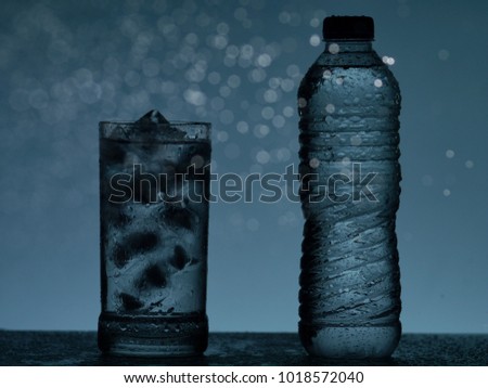 glass of water with ice next to a plastic bottle of water on blue background