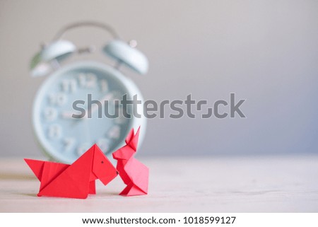 Creative lay out.Red dog and rabbit paper origami with blur alarm clock in background. Dog and rabbit origami with copy space.Chinese New Year concept. Selective Focus shot.