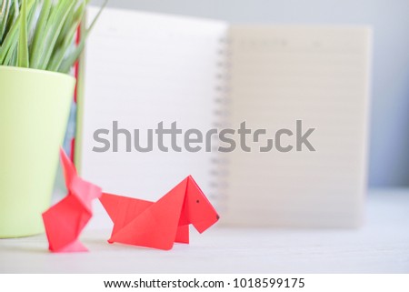 Creative lay out.Red dog and rabbit paper origami with blur green tree and note book in background. Dog and rabbit origami with copy space.Chinese New Year concept. Selective Focus shot.