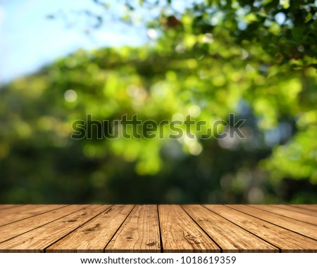Brown wood surface on a green background. Green leaf background, blurred sun, abstract bokeh can be used for displaying or editing your product.