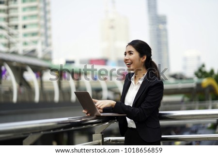 Young business woman working with laptop outdoor and  modern city background. Happy Business woman with computer laptop thinking looking up at copy space in business district. Asian  Caucasian woman