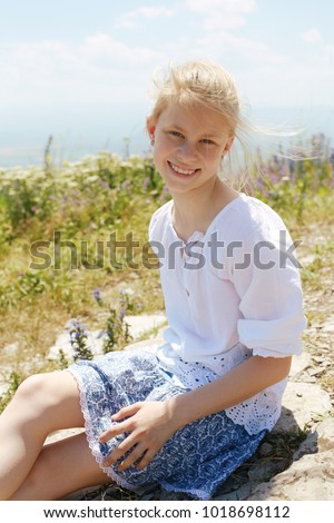 Concept of happiness. Cute happy  child in white blouse on a rock with raised hands and looking to a valley below