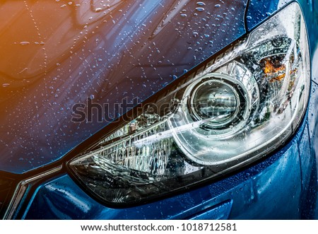 Closeup headlamp of blue car are washing with water. Car care service business concept. Car wash service. Car covered with drops of water after cleaning with high pressure water spray. Auto care. Royalty-Free Stock Photo #1018712581